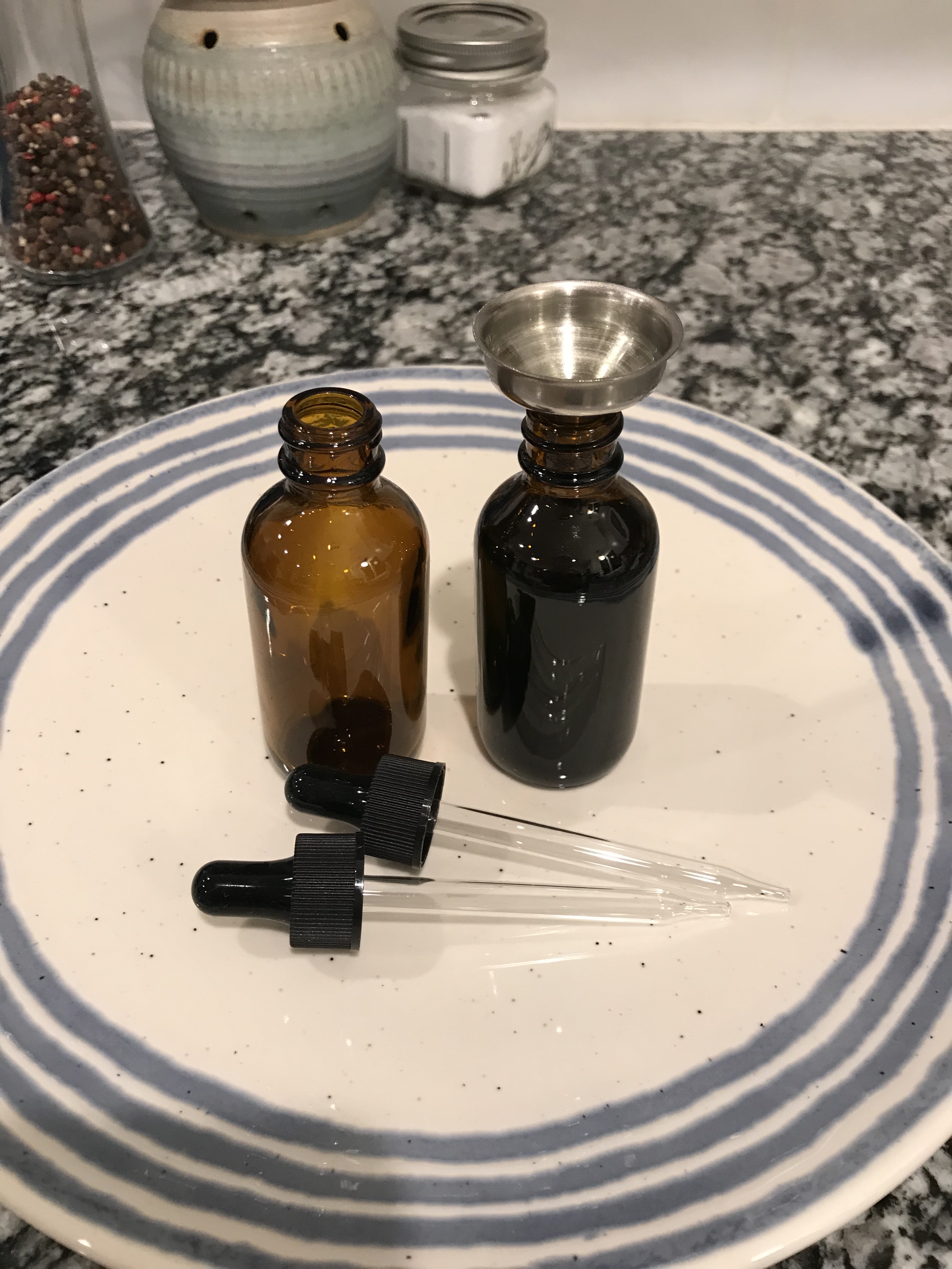 A tiny funnel is very useful when pouring the infused coconut oil into a glass bottle with dropper. Notice the plate beneath the bottles, in case anything spills.
